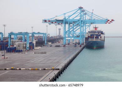 Men load big cargo boat docked to industrial port with blue cranes