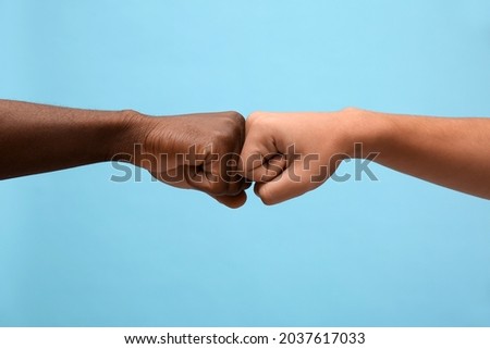Men making fist bump on light blue background, closeup