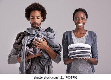 Men Are From Mars.... Studio Shot Of A Woman Holding A Neatly Folded Pile Of Clothes While Her Partners Is In A Mess.