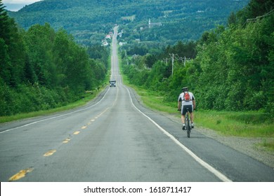 A Men On A Long Bike Journey Rides Along The Side Of An Asphalt Road In The Countryside