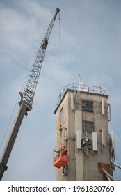 Men In Orange Crane Cage Basket High Above The Ground Working On Concrete Tower For Cell Phone Network In Goldendale Washington