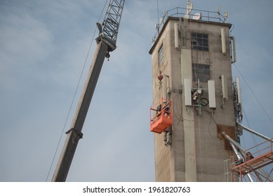 Men In Orange Crane Cage Basket High Above The Ground Working On Concrete Tower For Cell Phone Network In Goldendale Washington