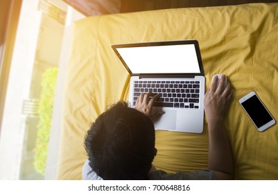 Men are playing computer in bed, with smart phone lying next to him.