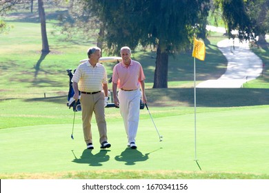 Men Playing On Golf Course Walk On Green With Flag Holding Golf Clubs