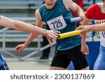 men relay race baton passing in summer athletics championship, close-up of athletes hands on background of runners