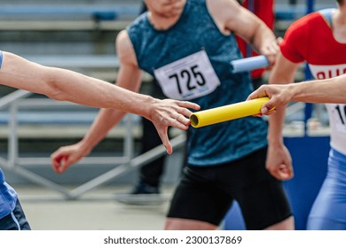 men relay race baton passing in summer athletics championship, close-up of athletes hands on background of runners - Powered by Shutterstock