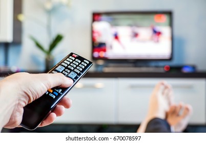 Men With The Remote Control Front Of The Television. A Man Is Relaxing On Sofa And Watching Sports On TV.