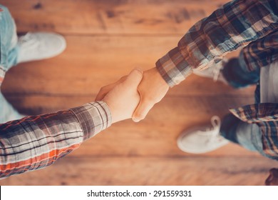 Men shaking hands. Top view of two men shaking hands while standing on the wooden floor