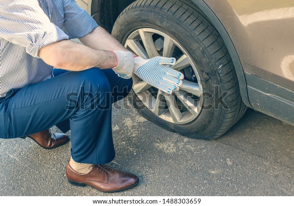 Men in a shirt\
of business suit putting on repair gloves for changing punctured\
wheel. Hole in the tire.\
Concept
