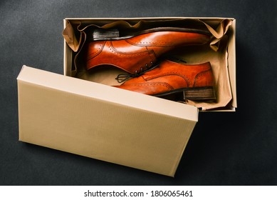 Men Shoes In An Open Box, Isolated On A Black Background. Open Shoe Box. New Shoes From The Store. Brown Shoes Made Of Genuine Leather. The View From The Top