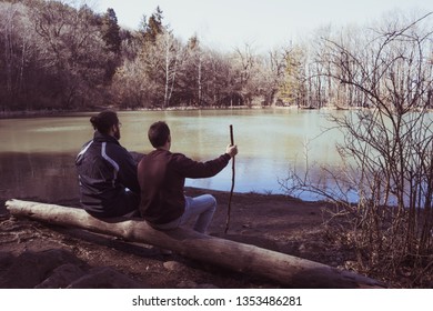 men sitting in a down tree in front of a lake in the forest without clouds