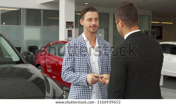 Men stand in the middle of the car dealership.\
They discuss the details of the deal. They shake hands. There was a\
car purchase
