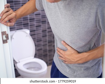 Men are standing in front of the bathroom door using their hands to hold the abdomen with severe abdominal pain or diarrhea. The concept of stomach cramps, diarrhea