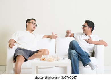 Men Talk Concept. Two Young Male Friend Sitting On Sofa And Chatting At Home. Multiracial People Friendship.