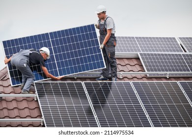 Men technicians carrying photovoltaic solar moduls on roof of house. Engineers in helmets installing solar panel system outdoors. Concept of alternative and renewable energy.