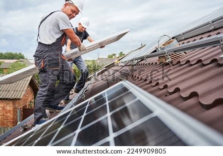 Men technicians carrying photovoltaic solar moduls on roof of house. Builders in helmets installing solar panel system outdoors. Concept of alternative and renewable energy. Stockfoto © 