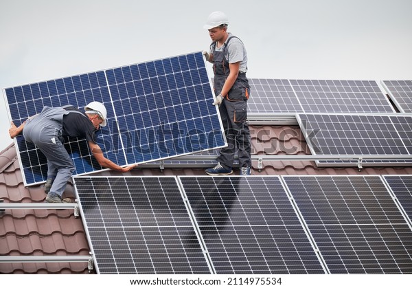 Men\
technicians carrying photovoltaic solar moduls on roof of house.\
Engineers in helmets installing solar panel system outdoors.\
Concept of alternative and renewable\
energy.