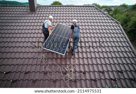 Men technicians lifting photovoltaic solar moduls on roof of house. Electricians in helmets mounting solar panel system outdoors. Concept of alternative and renewable energy. Aerial view.