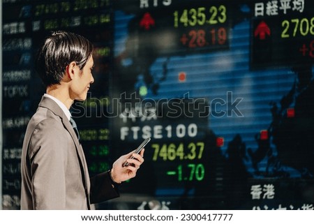 Men in their thirties in their thirties with a confident expression to confirm the stock price of the world on the world map reflected on the electronic bulletin board with a smartphone in hand