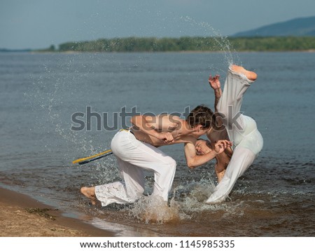 Men train capoeira on the beach - concept about people, lifestyle and sport. Training of two fighters in the water