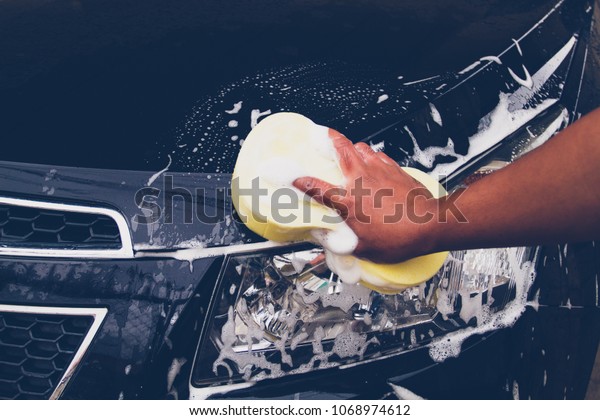 Men use a yellow\
sponge to wash the car