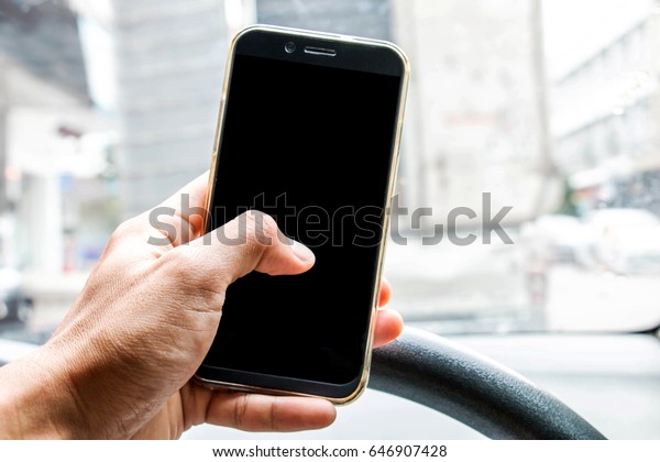 Men are using\
the mobile phone while driving on the road. Close-up of hand using\
mobile phone on control\
wheel.