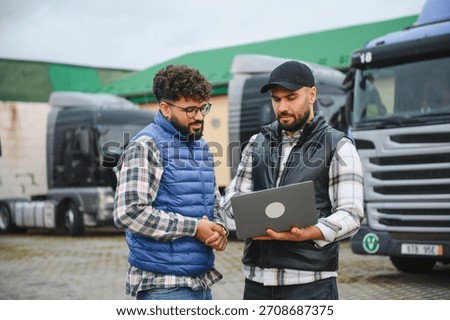 Men in vests shaking hands, finalizing a business deal in transportation logistics, with a truck fleet in the background