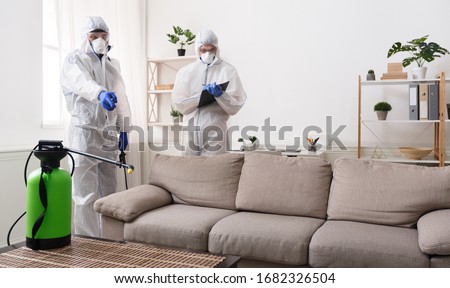 Men in virus protective suit making treatment of sofas and surfaces from coronavirus, preventive measures, copy space
