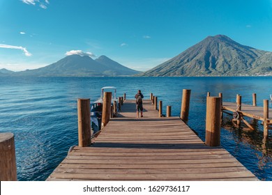 Men Walking Along Jetty At Lake Atitlán Looking San Pedro Volcano And Atitlán Volcano, Guatemala