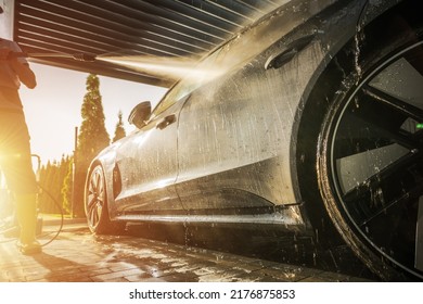 Men Washing His Car Using Pressure Washer Inside A Modern Carport During Scenic Sunset