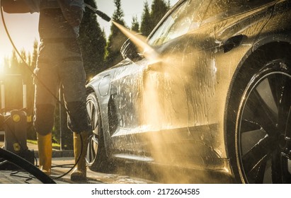 Men Washing His Modern Luxury Car Using Powerful Pressure Washer During Sunset. Automotive Maintenance Theme.