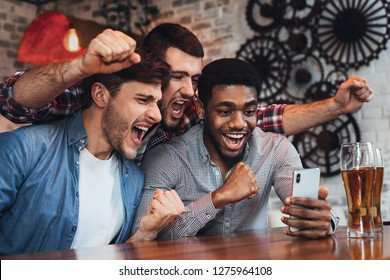 Men Watching Football On Smartphone And Drinking Beer In Bar