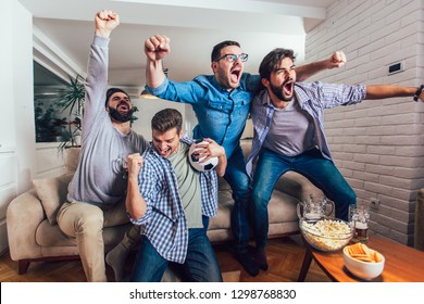 Men Watching Sport On Tv Together At Home Screaming Cheerful. Group Of Friends Sitting On The Couch And Watching A Football Game.