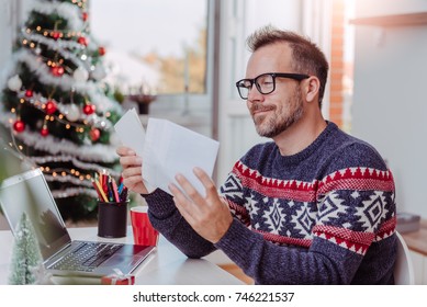 Men wearing blue sweater and eyeglasses opening christmas letter