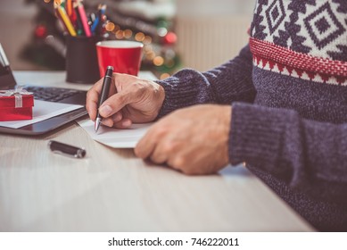 Men wearing blue sweater and eyeglasses writing christmas letter 