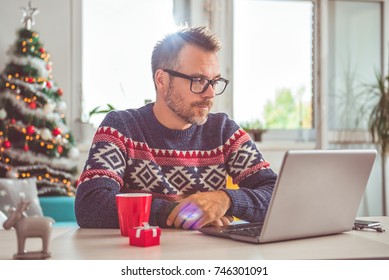 Men wearing blue sweater and eyeglasses using laptop at home office during christmas holidays - Powered by Shutterstock