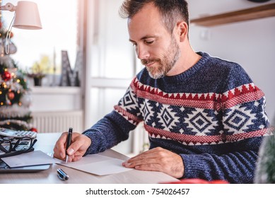 Men wearing blue sweater writing greeting cards at home office during christmas