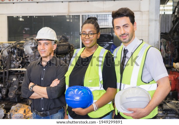 Men\
and woman work together, holding helmets and looking straight.\
Caucasian engineer manager men wear helmet, black woman and\
caucasian man holding helmets in\
factory-warehouse