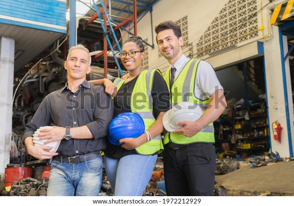 Men and woman work together,\
holding helmets and looking at left side. Caucasian engineer men\
and black woman holding helmets with act as smart in\
factory-warehouse