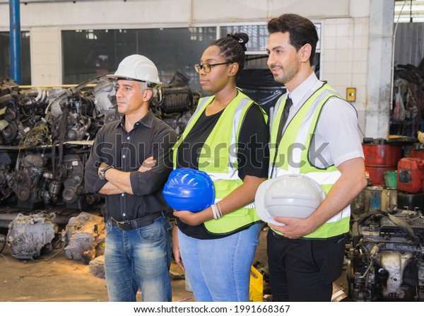 Men\
and woman work together, holding helmets and looking at left side.\
Caucasian engineer manager men wear helmet, black woman and\
caucasian man holding helmets in\
factory-warehouse