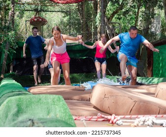 Men And Women Jumping On Floating Platforms To Reach Finish Of Water Obstacle Course. Family Resting In Amusement Park In Summertime.