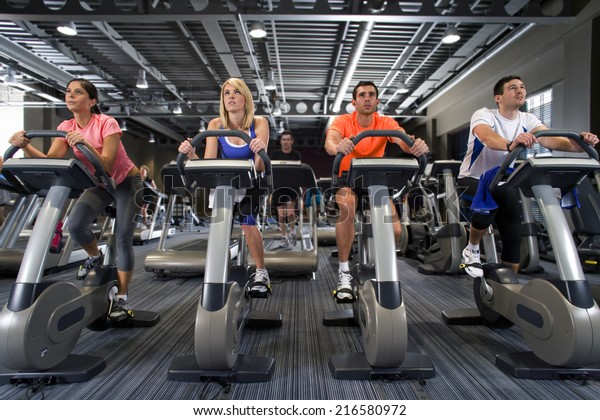 Men and\
women riding exercise bikes in health\
club
