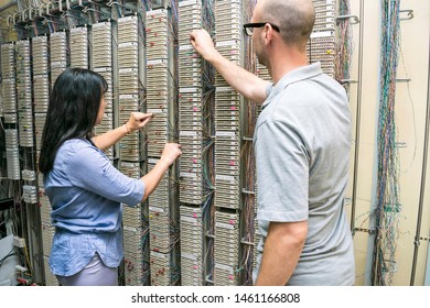 Men And Women Switch The Wires In The Network Switching Patch Of The IP Telephony Panel. Specialists Work In The Server Room. A Team Of People Is In The Data Center.