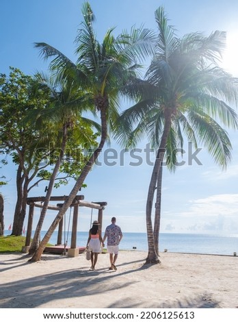 Men and women walking on a tropical beach with palm trees in Hua Hin Thailand. Asian women and European men on a tropical beach in Thailand