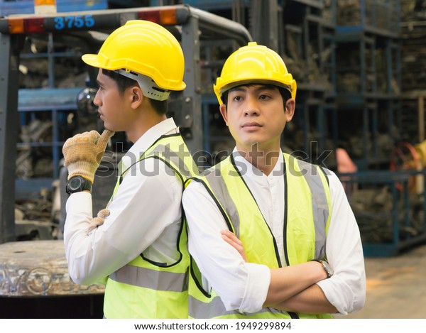 Men work together, Asian\
engineer worker men stand, crossed arms, and catch chin in\
factory-warehouse