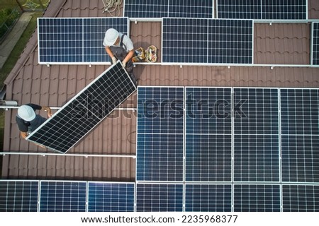 Men workers installing photovoltaic solar moduls on roof of house. Engineers in helmet building solar panel system outdoors. Concept of alternative and renewable energy. Aerial view.