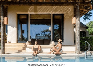Men working at a laptop a digital nomad working at a swimming pool during a vacation on a tropical island. man and woman in the infinity pool during sunset. luxury vacation in a luxury pool villa