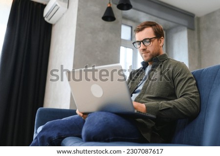 Men working on laptop computer in his room. Home work or study, freelance concept. Young man sitting relaxed on sofa with laptop. Modern businessman using laptop