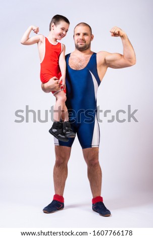 Men in wrestling tights  holds the boy with one hand and they both show bicepson a white isolated background. Dad and son have been fooling around forever.Teaching children Greco-Roman wrestling