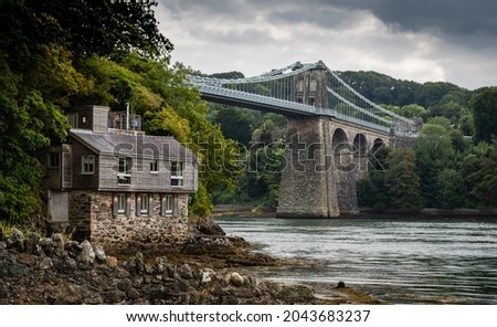 Menai suspension bridge in North Wales with boathouse in foreground on a gloomy day